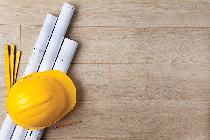 an image of a construction tools, a helmet, blueprints, pencil and measuring stick