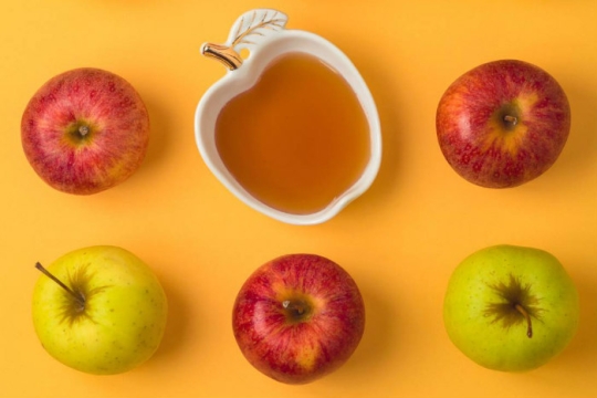 Flatlay of red and green apples and an apple shaped honey dish on a yellow surface 