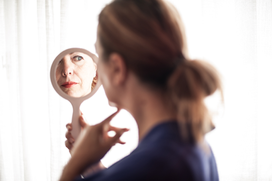 Photo of a woman looking at her reflection in a small hand-held mirrow